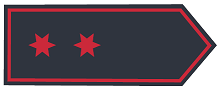 Schulterklappe in dunkelblauer Grundfarbe mit zwei sechszackigen Sternen in Rot, mittig in Reihe, Abzeichenumrandung in Rot
